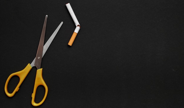 Бесплатное фото Ножницы и сломанная сигарета на черном фоне