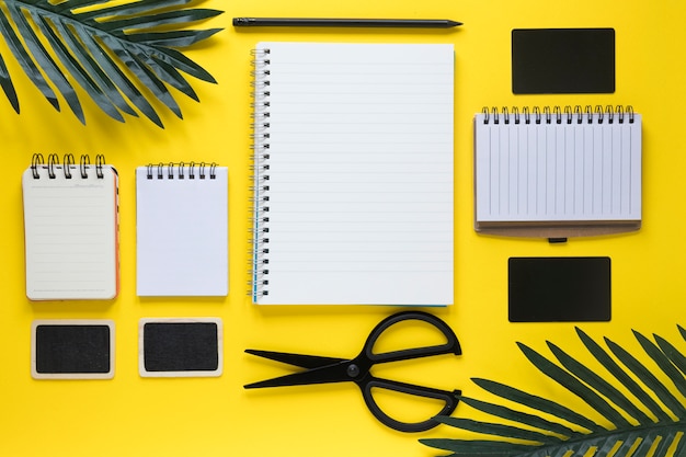 Free photo scissor; card; and pencil with different type of spiral notepads on yellow background