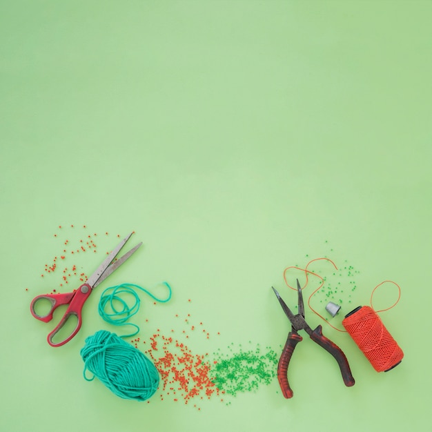 Free photo scissor; plier; wool; beads and an orange yarn spool on green background