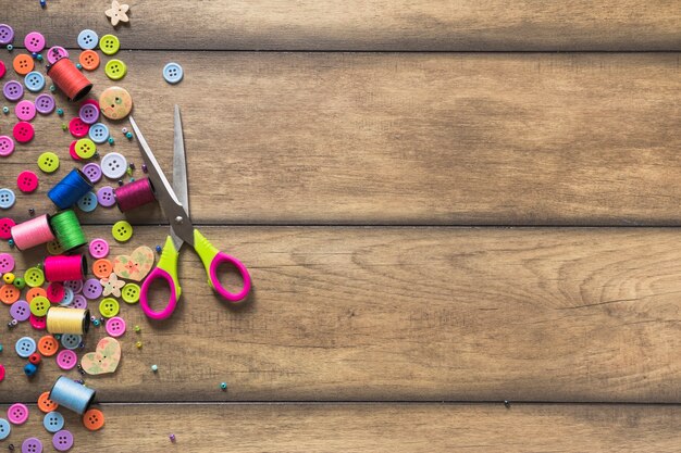 Scissor with colorful spools and buttons on wooden backdrop