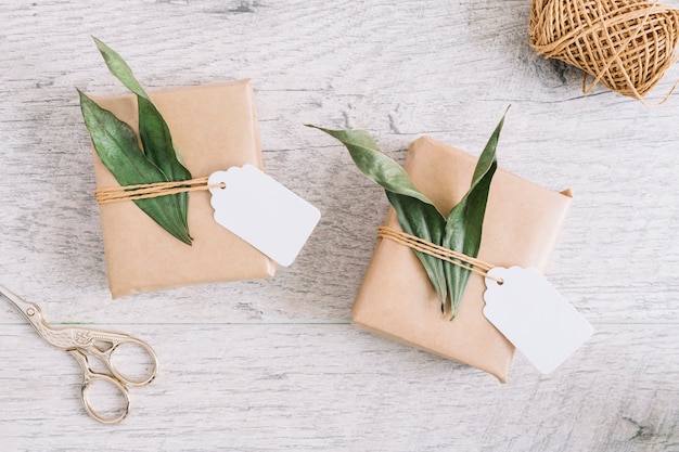 Scissor and wrapped presents with tag and leaves on wooden background