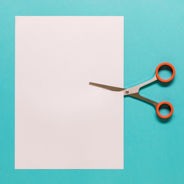 Scissors cutting paper on blue background