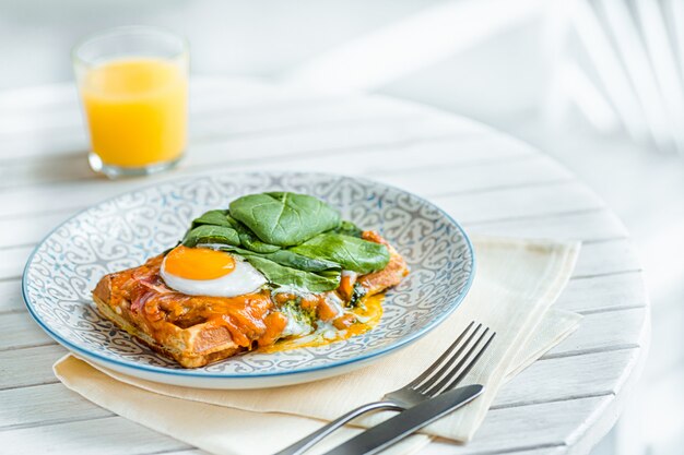 Scrambled eggs on meat with fried potatoes and toast at plate on wooden table