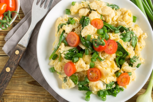 Premium Photo | Scrambled eggs with spinach and tomatoes on a white ...
