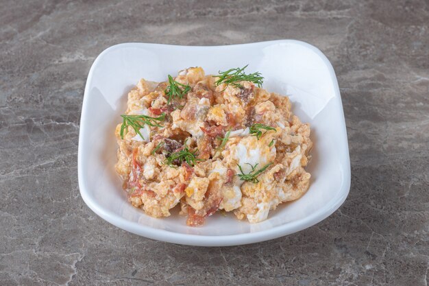 Scrambled eggs with various vegetables in white bowl.