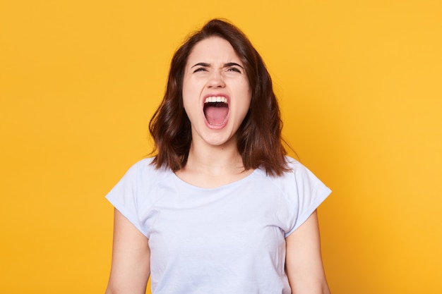 Screaming emotional angry woman poses isolated over yellow studio