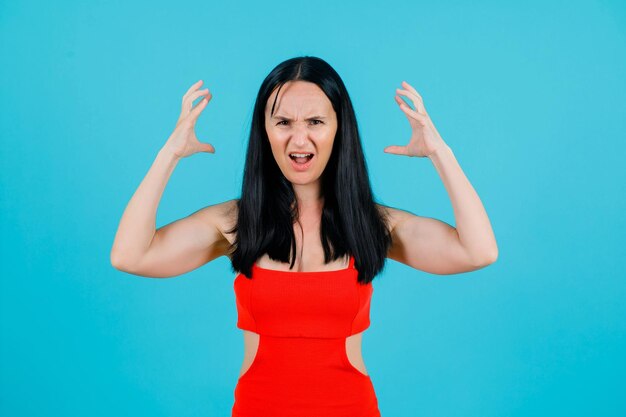 Screaming girl is holding hands near head on blue background