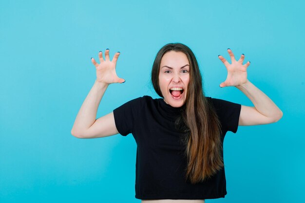 Screaming girl is showing claws gestures by raising up hands on blue background