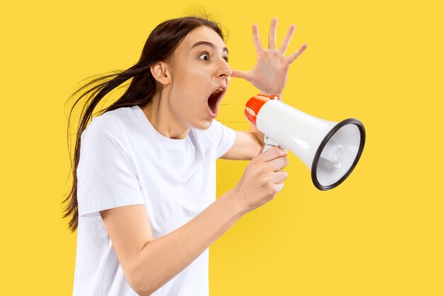 Screaming girl with the mouthpiece. Beautiful female half-length portrait isolated on yellow wall. Young smiling woman. Negative space. Facial expression, human emotions concept.