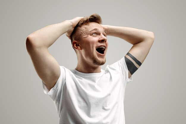 Screaming, hate, rage. Crying emotional angry man screaming on gray studio background. Emotional, young face. male half-length portrait. Human emotions, facial expression concept.