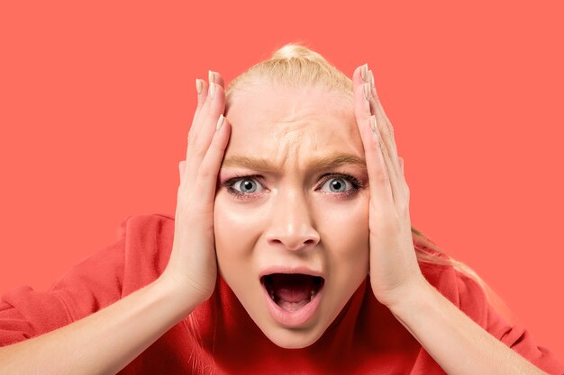 Screaming, hate, rage. Crying emotional angry woman screaming on coral studio background. Emotional, young face. Female half-length portrait.