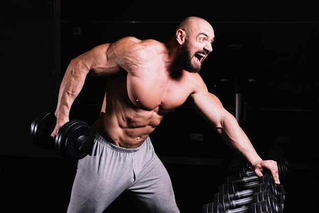 Screaming man lifting heavy dumbbell