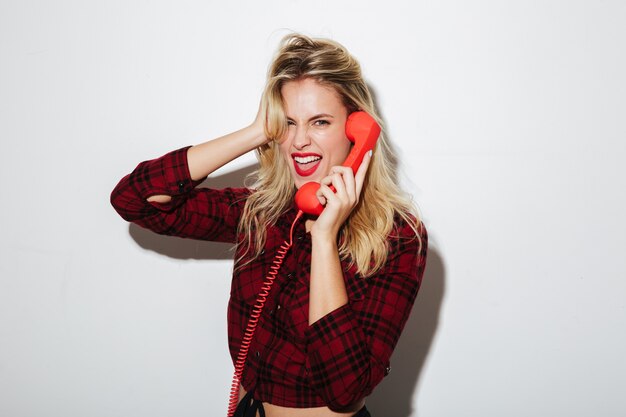 Screaming woman talking by red retro telephone.