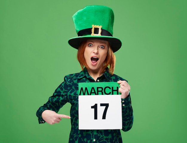 Free photo screaming woman with leprechaun's hat pointing at calendar