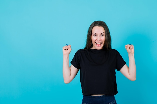 Screaming young girl is raising up her fists on blue background