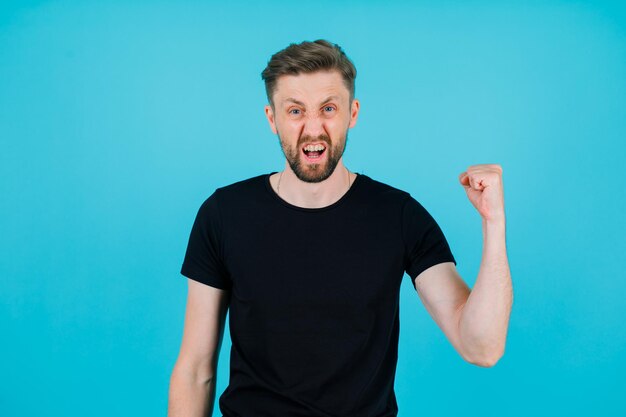 Screaming young man is raising up his fist on blue background