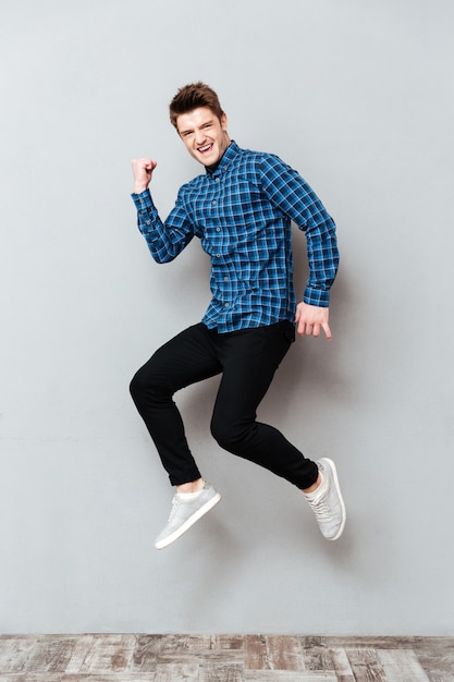 Free photo screaming young man standing over grey wall and jumping.