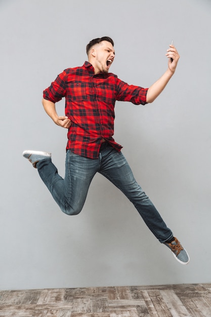 Screaming young man using mobile phone make winner gesture.