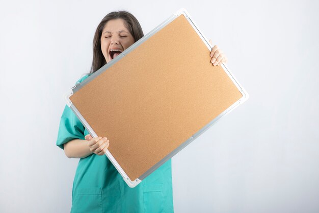 Screaming young medical worker holding a board with hands.
