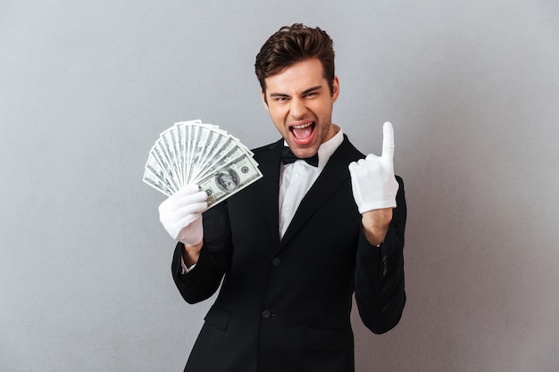 Free photo screaming young waiter pointing while holding money.