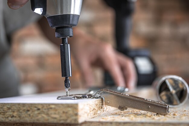 Вкручивание самореза в металлическое крепежное отверстие на деревянной планке с помощью отвертки, работа плотника.