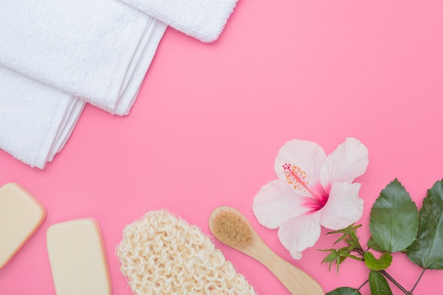 Scrub glove; brush; hibiscus flower; soap and towel on pink background