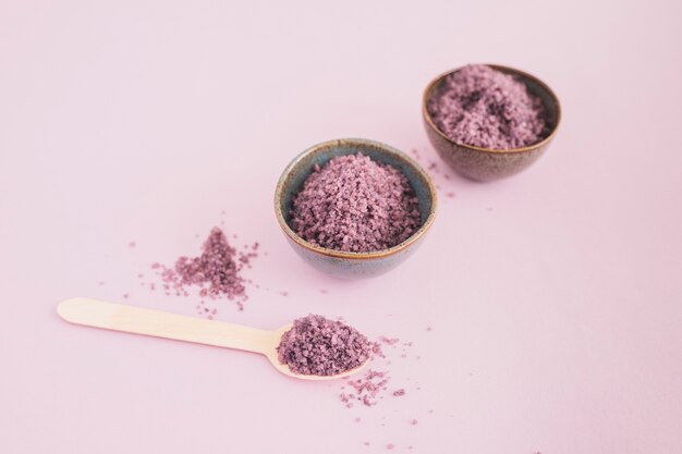 Sea salt in bowl and spoon on pink background