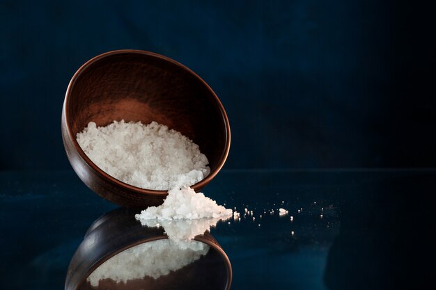 Sea salt in wooden bowl over black background.