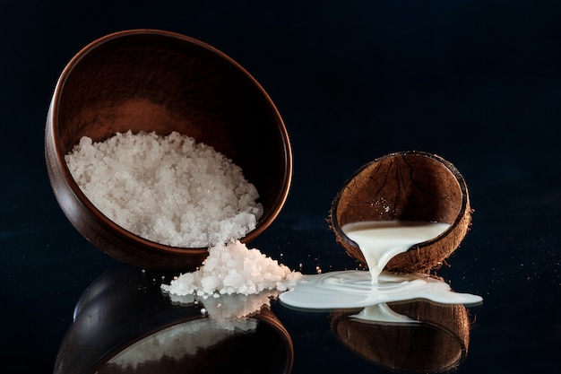 Sea salt in wooden bowl and coconut over black surface