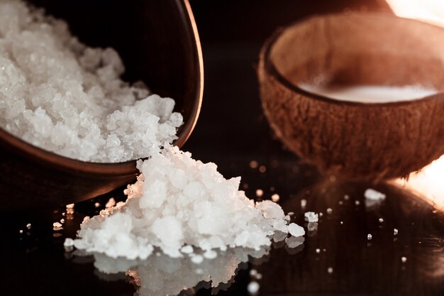 Free photo sea salt in wooden bowl and coconut over black surface