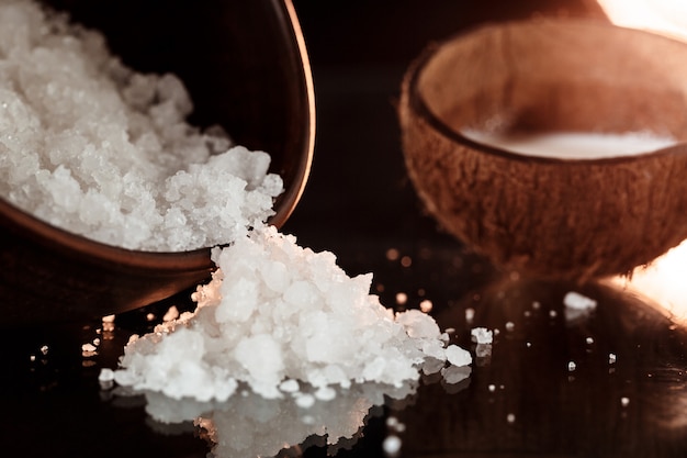 Sea salt in wooden bowl and coconut over black surface