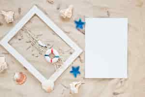 Free photo sea shells with frame and blank paper on sand