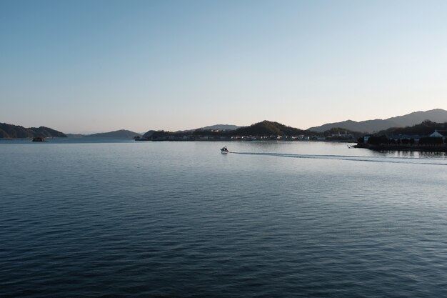 Sea surrounded by hills covered in buildings and greenery under a blue sky