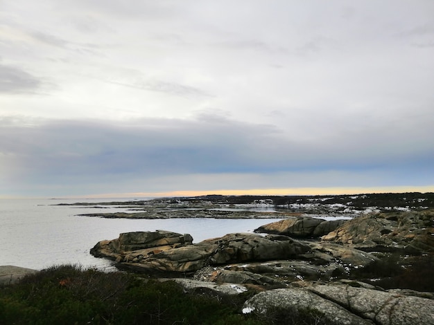 ノルウェーの日没時に曇り空の下で枝に覆われた岩に囲まれた海