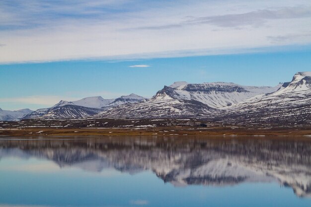Sea surrounded by rocky mountains covered in the snow and reflecting on the water in Iceland