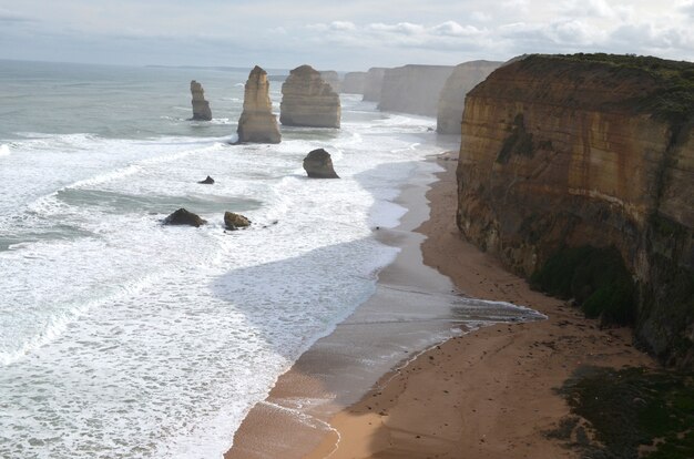 Sea waves hitting the shore with rocks near cliffs under a cloudy sky