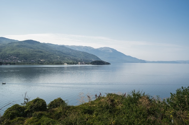 Free photo sea with boats on it surrounded by hills covered in greenery under sunlight