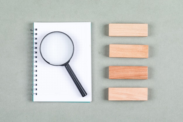 Searching and research concept with notebook, magnifier, wooden blocks on gray background top view. horizontal image