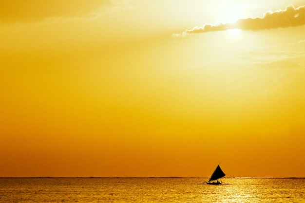 Морской пейзаж с золотым закатом и парусной лодкой посреди океана