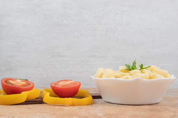 Seashell shaped pasta in bowl with pepper and tomato slices. 