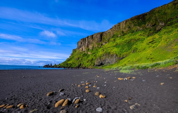 Spiaggia vicino a una collina erbosa e una scogliera con un cielo blu sullo sfondo