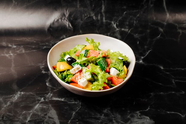Сезонный овощной салат со смешанными продуктами внутри белый шар на черном мраморе.