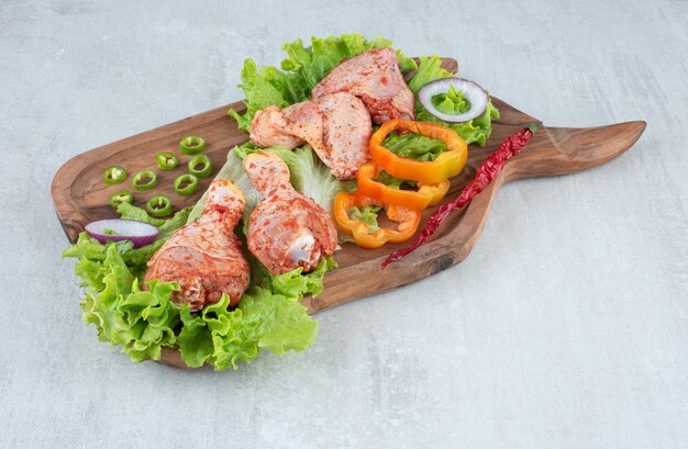 Seasoned chicken parts with vegetables on wooden board.