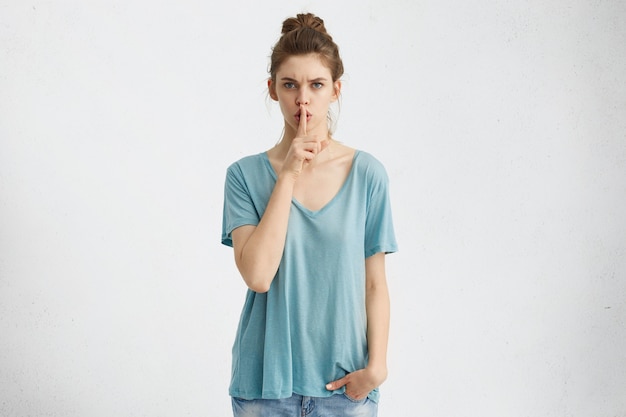Secrecy, privacy and confidentiality. Attractive young woman with serious strict look holding index finger at her lips, saying shh, demanding silence or asking to keep private information a secret