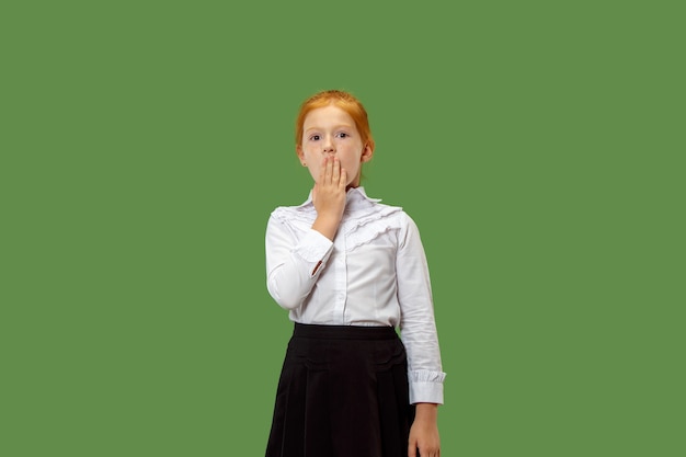 Secret, gossip concept. Young girl whispering a secret behind her hand. She isolated on trendy green studio background. Young emotional teen. Human emotions, facial expression concept.