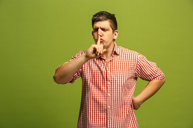 Secret, gossip concept. Young man whispering a secret behind his hand. Businessman isolated on trendy green studio background. Young emotional man. 