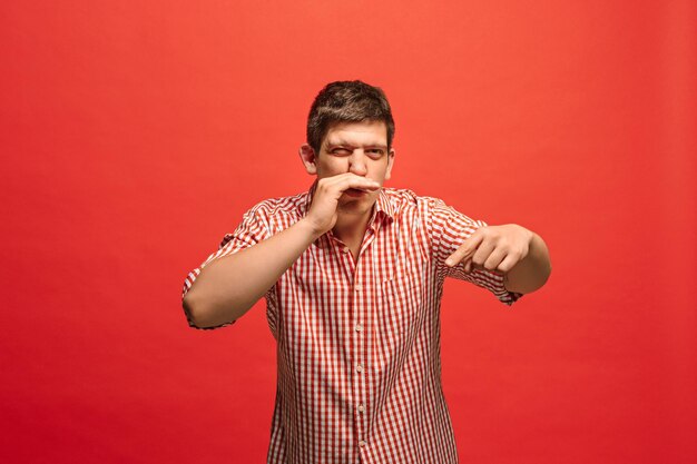 Secret, gossip concept. Young man whispering a secret behind his hand. Businessman isolated on trendy red studio background. Young emotional man. 