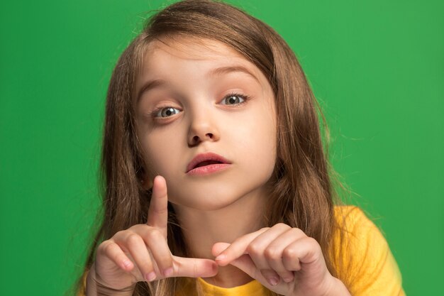 Secret, gossip concept. Young teen girl whispering a secret behind her hand isolated on trendy green studio background