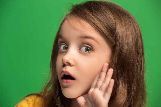 Secret, gossip concept. Young teen girl whispering a secret behind her hand isolated on trendy green studio