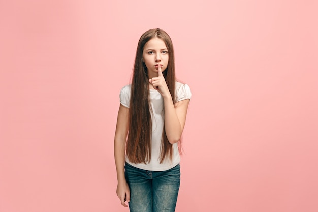 Secret, gossip concept. Young teen girl whispering a secret behind her hand isolated on trendy pink studio background.